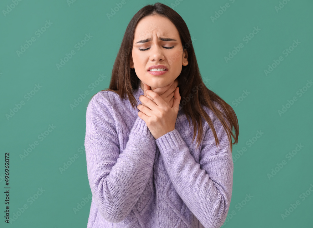 Young woman having sore throat on green background