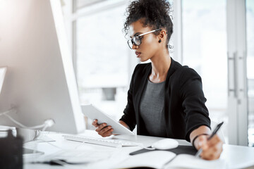 Aufkleber - Productivity = success. Shot of a young businesswoman using a digital tablet, computer and writing notes at her desk in a modern office.