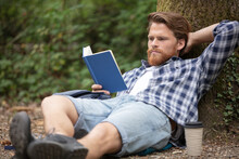 Man Reading Book In Park Sitting Under A Tree