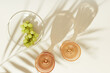 © yrabota - Two glasses of white wine from pale pink colored glass with palm leaf shadow from sunlight and plate with grapes fruit, summer drink minimal concept, modern glass on peach color background