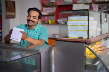 Wall Mural - Portrait of happy Sweet shop owner maintaining accounts at counter