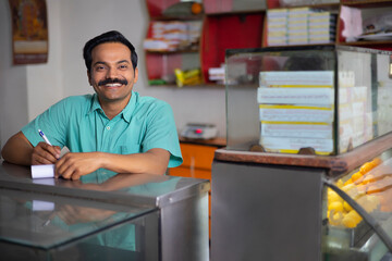 Wall Mural - Portrait of Sweet shop owner looking at camera with smile while maintaining accounts at counter