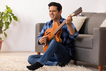 Wall Mural - Portrait of a young musician playing guitar in living room