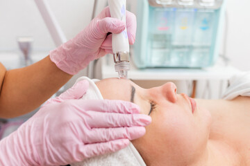 Wall Mural - Beauty salon. The cosmetologist in medical gloves doing a water peeling procedure on the client's forehead. The concept of professional skin care