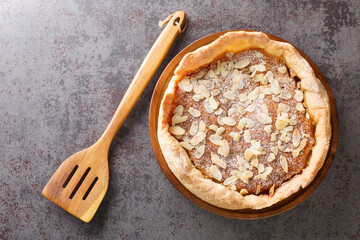 Bakewell Pudding is a sweet tart, a crisp pastry case filled with sweet almond sponge over raspberry jam closeup on the table. Horizontal top view from  above