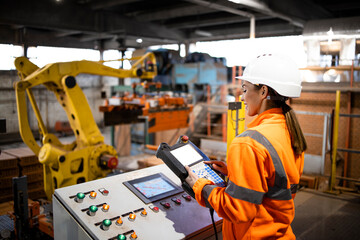 female factory worker operating industrial robot machine and observing manufacturing process in prod
