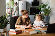 © AnnaStills - Young mother sitting at table with books together with her son and teaching him, she preparing him for school