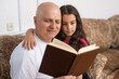 © Angelov - Happy grandfather and granddaughter reading book together at home. Close up.