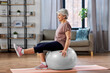 © Syda Productions - sport, fitness and healthy lifestyle concept - smiling senior woman training by sitting on exercise ball at home