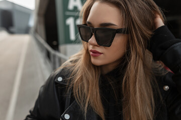 Wall Mural - Street female portrait of young pretty woman with fashion sunglasses in black leather jacket walks in the city