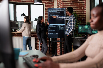 African american back end network developer explaining to coworker application lines of code. Team developing additional layers of security in order to sustain good functionality of system.