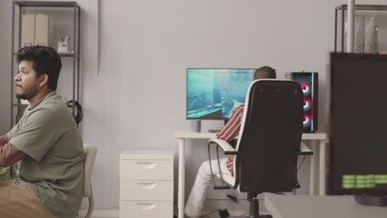 PAN slowmo of diverse team of programmers developing video games on pc in office, typing program codes and checking art, design and audio assets for bugs