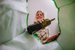© Halfpoint - Image from inside green recycling bag of woman throwing a glass bottle to recycle.