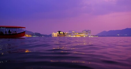 Fototapete - Famous luxury Udaipur Lake Palace Jag Niwas on island on lake Pichola on sunset - Rajput architecture of Mewar dynasty rulers of Rajasthan. with passing tourist boat. Udaipur, Rajasthan, India