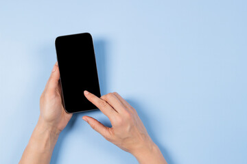 Female hand touching smartphone display and pointing with index finger on blank mobile phone screen on light blue background