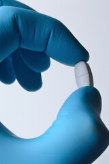 Wall Mural - a hand in a blue medical glove holds a white pill. close-up