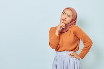 Portrait of beautiful young Asian Muslim woman in brown sweater, holding chin and looking seriously thinking question and looking at copy space isolated on white background. Muslim lifestyle concept