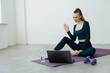 © F8  \ Suport Ukraine - Online Exercise Session Marathon, Remote Training. Happy millennial female sitting on floor mat and talking with coach, having videocall with teacher, using pc for virtual workout