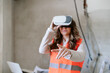 © Eva - architect woman in construction site using virtual reality goggles working on VR blueprints