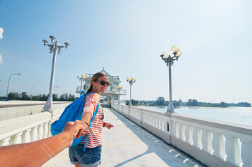 Wall Mural - Follow me. Travel concept. Vacation on Phuket island. Back view of young woman holding boyfriend's hand enjoying sea view from bridge terrace.