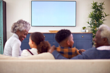 Wall Mural - Rear View Of Grandparents With Grandchildren Sitting On Sofa Watching Movie On TV At Home