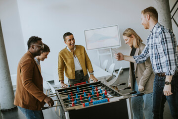 Wall Mural - Young casual multiethnic business people playing table football and relaxing at office