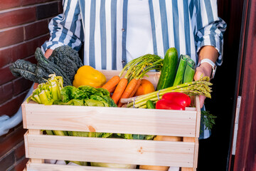 Wall Mural - Home food delivery. No face woman holding wooden box with fresh vegetables and fruits. Local farmer healthy food. Healthy dieting, weight loss concept. Online food order. Recipe box. Selective focus.