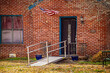 Metal handicap ramp built out from front porch of brick house with American flag flying on winter day
