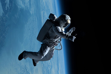 Wall Mural - female astronaut having a video call on her phone while performing spacewalk in deep space, earth in