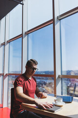 Smart software developer sitting at desktop in coworking space with laptop and creating publishing idea, using netbook for messaging and networking during freelance work