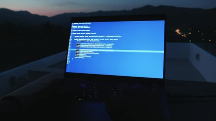 POV first-person portrait programmer developer programmer freelancer writes blue code at a laptop outside the office on tropical mountains background in the night