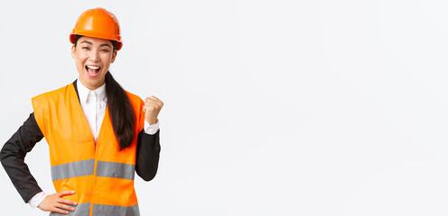 Successful businesswoman, construction manager in safety helmet, fist pump and say yes. Female asian architect celebrating great news, achieve goal at building zone, white background