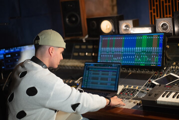 Young music producer working in sound recording studio. Sound engineer sitting at laptop and mixing console panel. Creating music concept