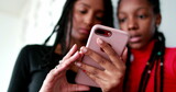 Fototapeta  - Black teenage girls holding smartphone device. African siblings looking at cellphone screen