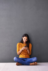 Canvas Print - Sending some love out into the world. Shot of an attractive young woman using a mobile phone while sitting on the floor.