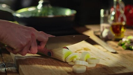 Wall Mural - Woman slicing leek and vegetables for cooking on kitchen table. Closeup hands. Cosy dark room.