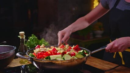 Wall Mural - Woman cooking frying meat and vegetables in wok pan on kitchen table. Closeup hands. Real, authentic cooking.