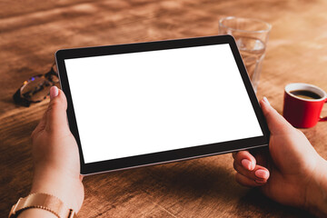 Woman’s hands holding tablet with blank screen. Wooden table (desk) as background. Free copy space.