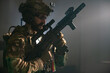 © KAMPUS - Attentive bearded man in military equipment in dark room. Man in uniform holding machine gun, getting ready for combat. Military, army, airsoft concept
