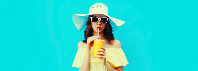 Portrait of beautiful young woman drinking a fresh juice wearing a summer hat on blue background