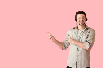 Poster - Smiling consultant of call center in headset pointing at something on pink background