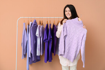 Sticker - Young Asian woman and rack with clothes in purple shades on beige background