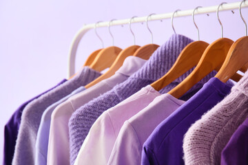 rack with clothes in purple shades on lilac background, closeup