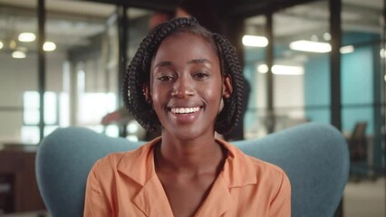 A young african teacher is sitting on the chair in the university, smiling and looking at the camera, slow motion close-up