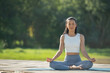 © sutlafk - Woman on a yoga mat to relax in the park at mountain lake. Calm woman with closed eyes practicing yoga, sitting in Padmasana pose on mat, Lotus exercise, attractive sporty girl in sportswear.