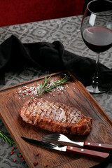 Wall Mural - Grilled New york or striploin beef steak served with seasonings, herbs and a glass of wine on a wooden board. Cooking steak on the grill