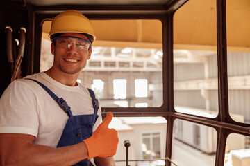 Wall Mural - Cheerful young man sitting in operator cabin and giving thumbs up