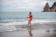 © svetograph - A beautiful and sexy brunette in a red swimsuit on a pebble beach, Running along the shore in the foam of the waves