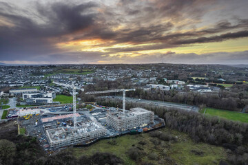 Construction site with two tall cranes by a green zone of a city. Dramatic sky. Developing residential and office building. Building in urban area. Modern technology.