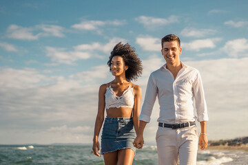 Portrait of multiracial young couple walking hand to hand in the beach in a sunny day on summer - travel and vacation concept